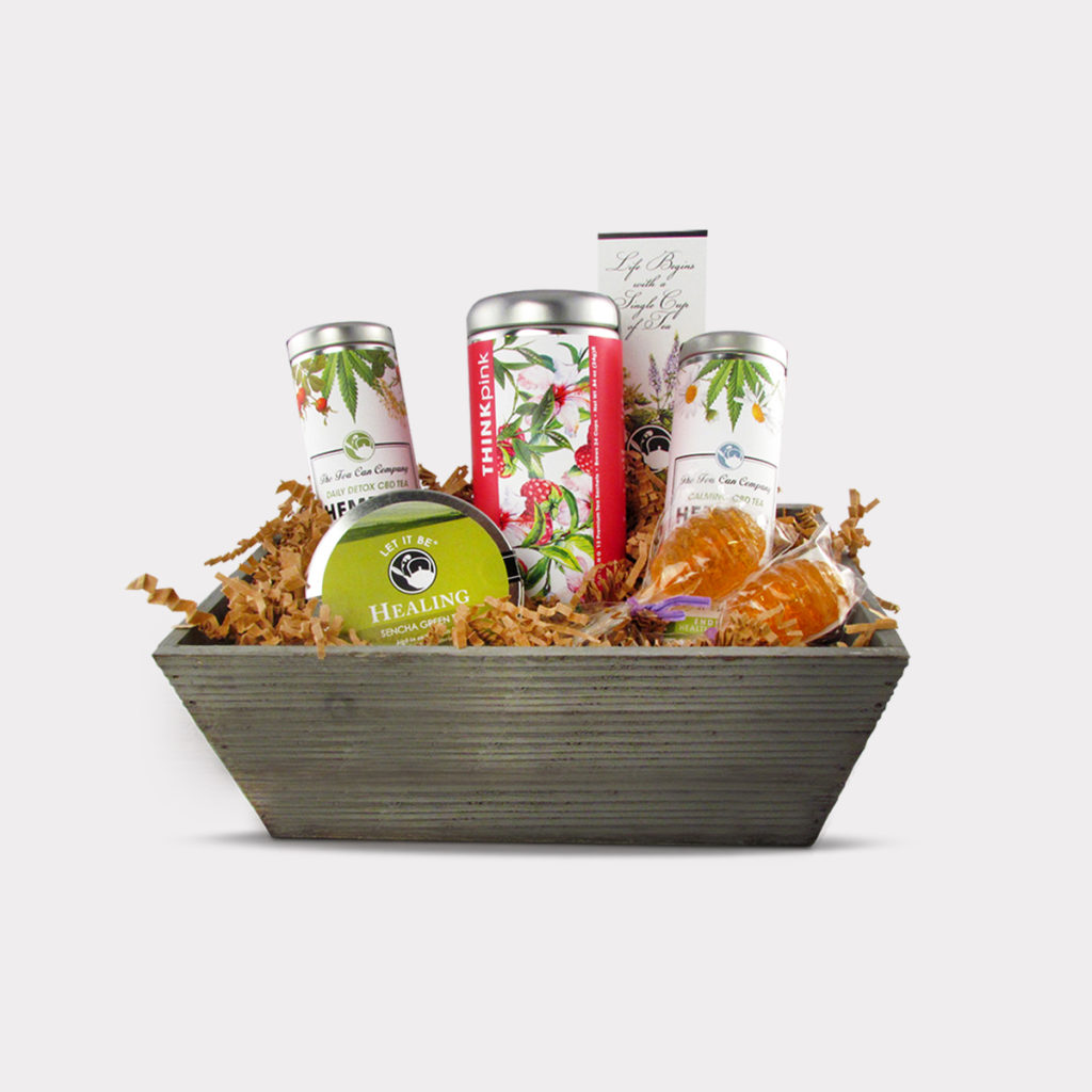 HEMPTEA™ Fundraising Breast Cancer Tea GiftBasket Gift Set in a decorative basket containing 1 Skinny Tin of High Strength Garden Blend HempTea™, 1 Skinny Tin of High Strength Chamomile Blend HempTea™, 1 Tall Tin of Raspberry Oolong Tea, 1 Mini Tin of Sencha Green Tea, 2 Honey Lollipop Stirrers, and 1 Tea Bookmark